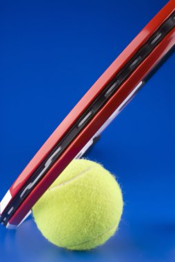 Tennis ball is next to a part of a tennis racket on a blue backg clipart