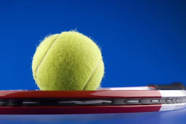 Pelota de tenis y raqueta de tenis sobre fondo azul . — Foto de Stock