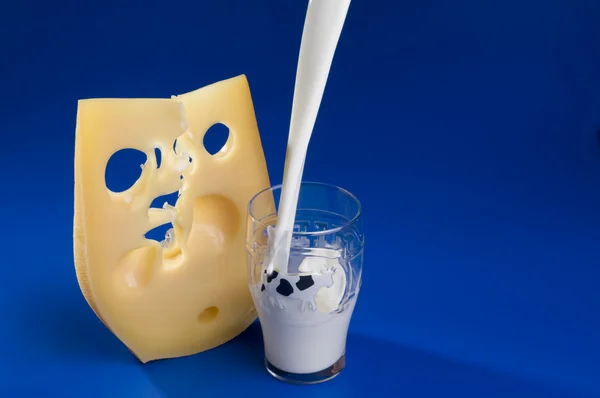 Pouring milk and cheese over blue background. — Stock Photo, Image