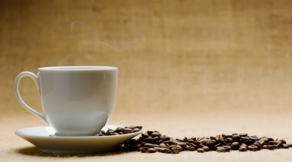 Xícara de café quente sobre a balsa e grãos de café no grunge — Fotografia de Stock