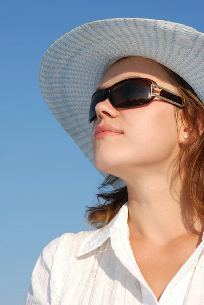 De vrouw in bril en een hoed op een achtergrond van de hemel — Stockfoto