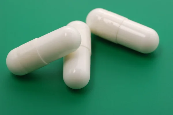 Белые таблетки на зеленом фоне — стоковое фото