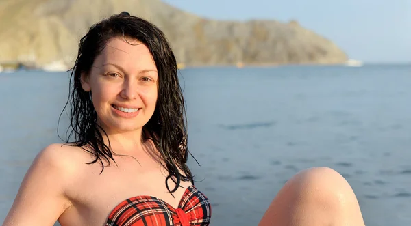 ผู้หญิงที่มีความสุขนั่งอยู่บนชายฝั่งทะเล — ภาพถ่ายสต็อก