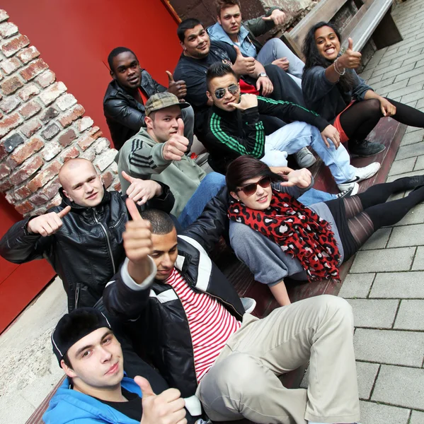 Diez jóvenes se sientan juntos y levantan el pulgar . — Foto de Stock