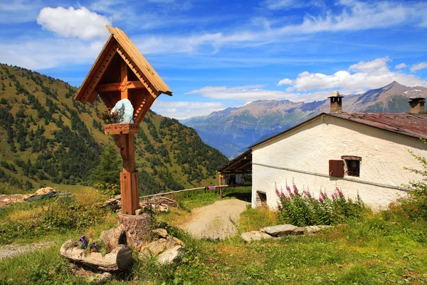 Dřevěný kříž poblíž venkovský dům v Alpách. — Stock fotografie