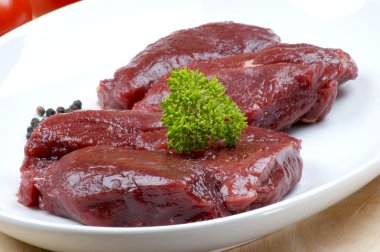 Raw ostrich steak with parsley on a plate clipart