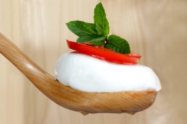 Mozzarella peyniri, domates ve bir tahta kaşıkla üzerine nane