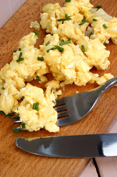 Huevos revueltos con cebollino, cuchillo y tenedor en una tabla de madera —  Fotos de Stock