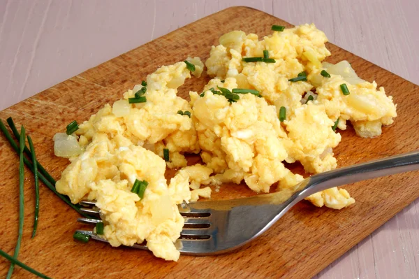 Scrambled eggs with chives and knife on a wooden board — Stock Photo, Image