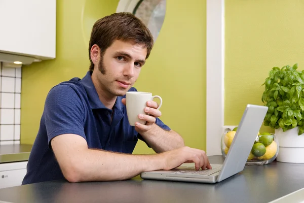 Jonge man met warme drankje op computer — Stockfoto