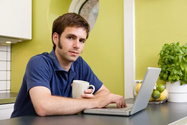 Młody człowiek z ciepłego napoju na komputerze — Zdjęcie stockowe
