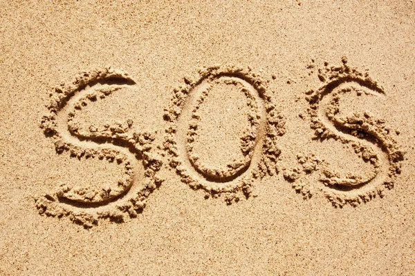 S.O.S escrito na areia de uma ilha com o oceano à distância — Fotografia de Stock