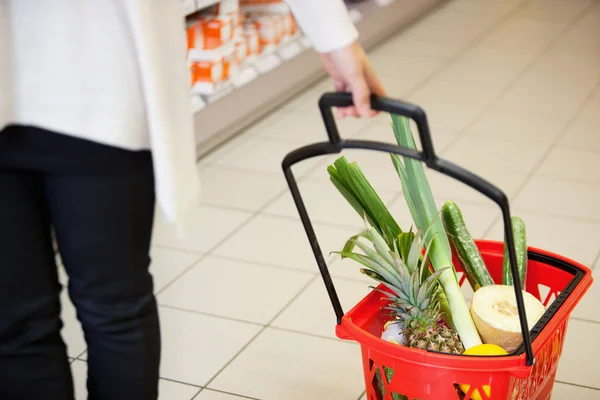Mulher puxando cesta de compras na mercearia — Fotografia de Stock