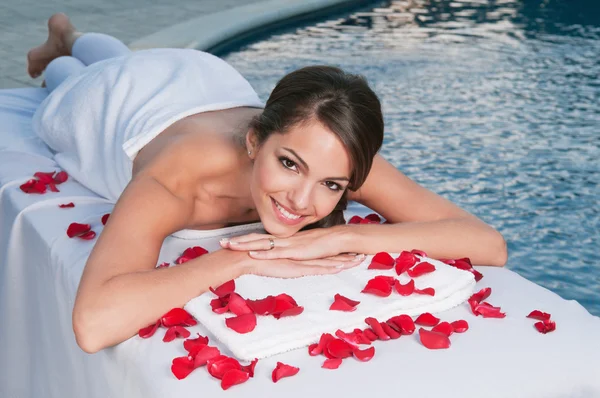 Uśmiechnięta młoda kobieta w spa z płatkami róż wokół — Zdjęcie stockowe