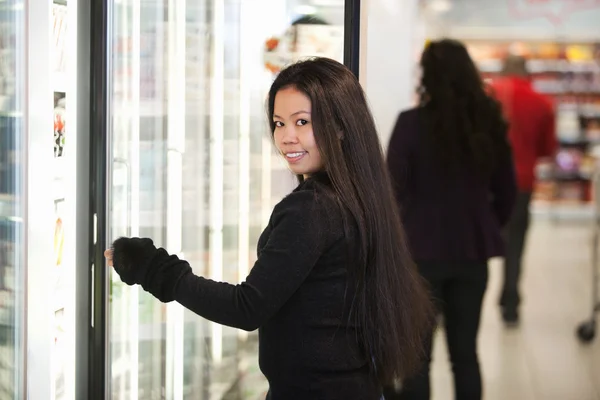 Fiatal nő mosolyogva, miközben megnyitása hűtőszekrény szupermarketben — Stock Fotó