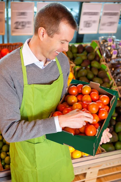 Happy market assistant holding box of tomatoes — Stock Photo, Image