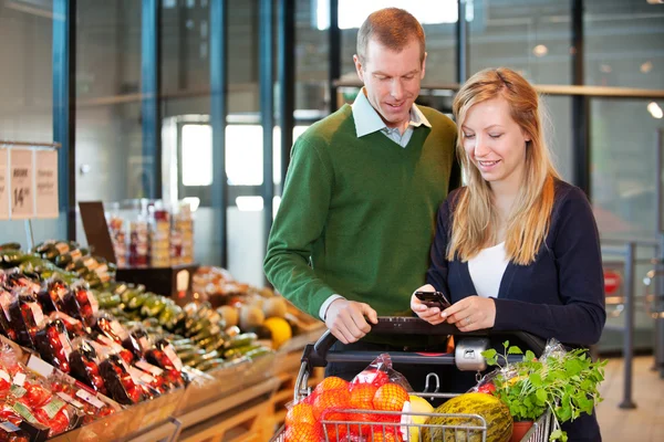 Pareja compra de comestibles con lista en el teléfono — Foto de Stock