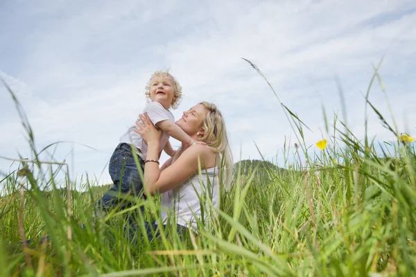 Mother sitting on grass while playing with boy — Stock Photo, Image