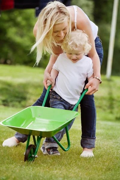 Mother helping her kid in pushing wheelbarrow — Stock Photo, Image