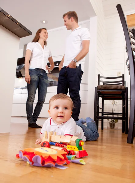 Baby spielt auf dem Boden mit Eltern im Hintergrund — Stockfoto