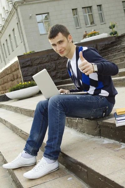 Un joven estudiante trabajando en un portátil. Pulgar hacia arriba —  Fotos de Stock