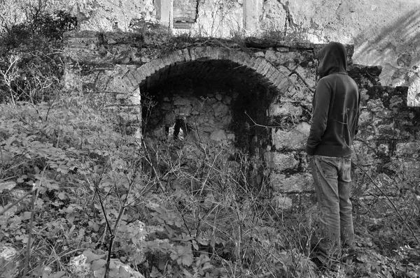 Hombre encapuchado junto al arco de la ruina rural — Foto de Stock