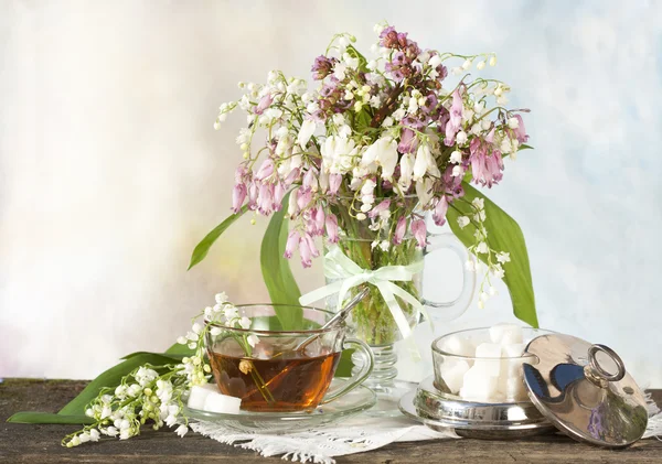 Tea in a cup and lilies of the valley — Stock Photo, Image
