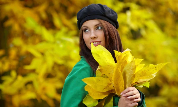 Fashion woman in autumn park holding yellow leaf — Stock Photo, Image