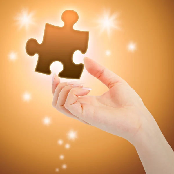 Womanish hand with a orange shining piece of puzzle — Stock Photo, Image
