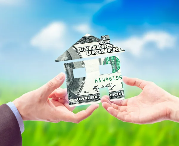 Дом из доллара США в руке против солнечного голубого неба — стоковое фото