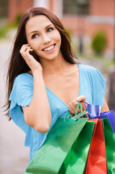 Młoda kobieta uśmiechający się do zakupów i telefon. — Zdjęcie stockowe