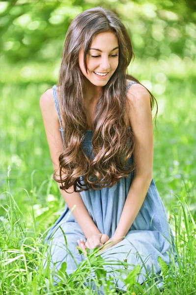 Yeşil çimenlerin üzerinde gülümseyen kadın oturur — Stok fotoğraf
