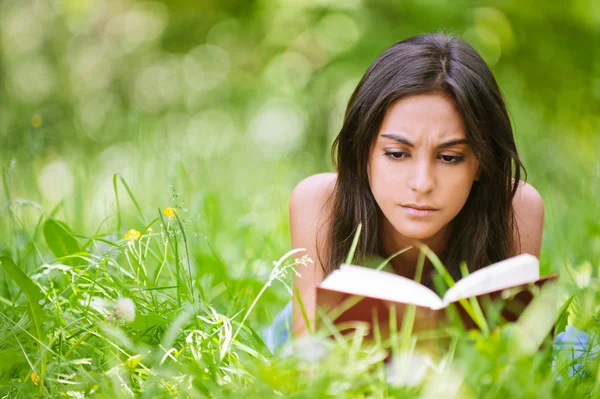 Жінка лежить на траві і читає книгу — стокове фото