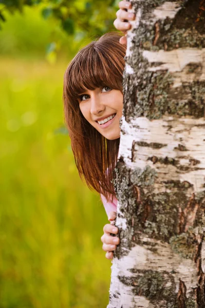Portret van lachen meisje op zoek achter de boom — Stockfoto