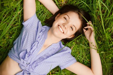 Portrait of young brunette woman lying on grass at summer green clipart