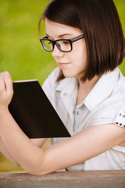 Симпатичная девушка в очках читает интересную книгу. — стоковое фото