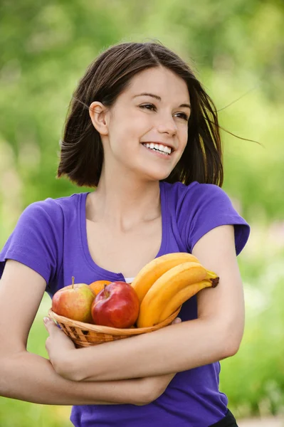 Mladá usměvavá žena drží košík s ovocem — Stock fotografie