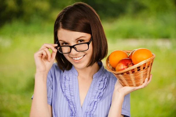 Joven mujer alegre con gafas sosteniendo cesta con frutas —  Fotos de Stock