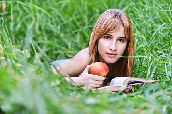 Νέα γυναίκα που κρατά την apple και την ανάγνωση του βιβλίου — Φωτογραφία Αρχείου