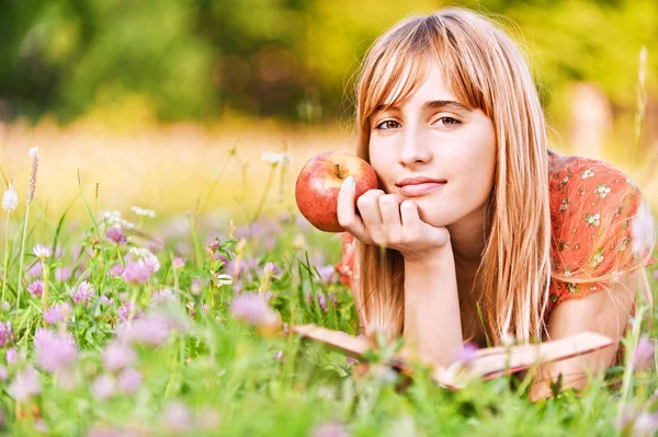 Ung kvinna med äpple och läsa bok — Stockfoto