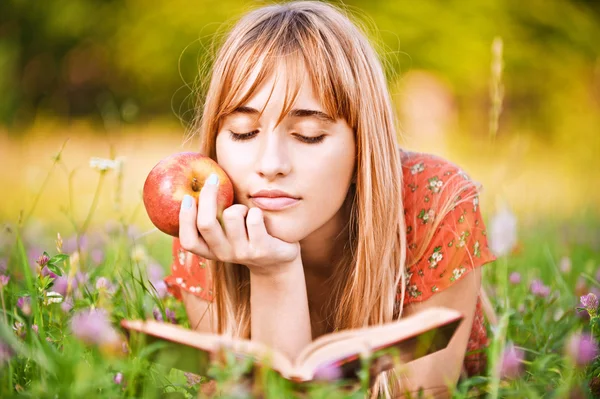 Mujer joven sosteniendo manzana y leyendo libro — Foto de Stock