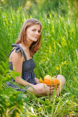 Portrait of young woman sitting in grass with basket full with f clipart