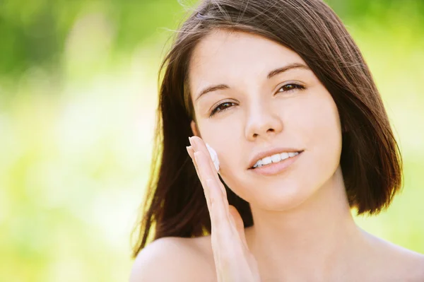 Portrait of young attractive woman putting cream on her face — Stock Photo, Image