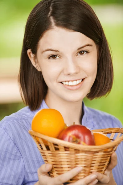 Портрет молодой улыбающейся брюнетки, держащей корзину с фруктами — стоковое фото