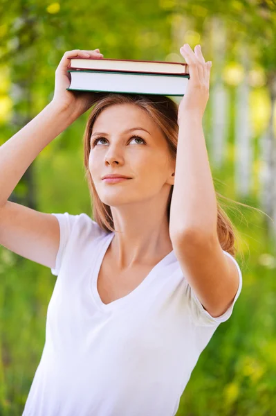 Portrait of young woman holding books on her head — Stock Photo, Image