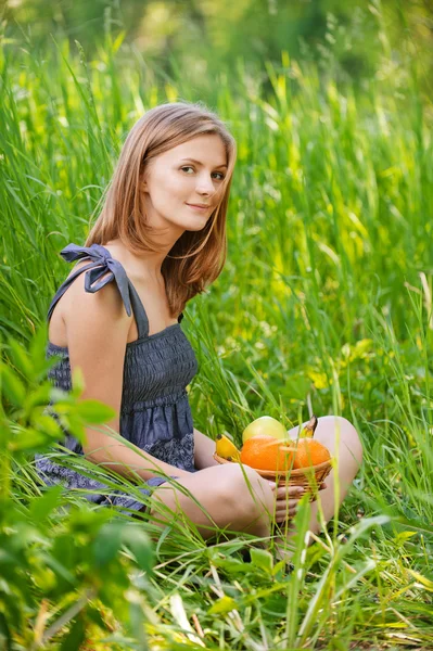 Portret młodej kobiety siedzi w trawie z koszem pełnym f — Zdjęcie stockowe