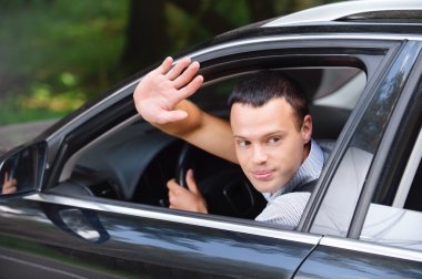 Portrait of young man driving car and greeting somebody with han clipart