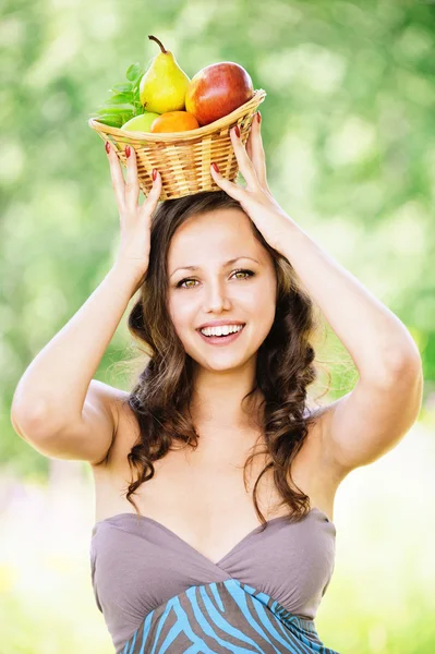 Portrait of young brunette woman holding basket full of fruits o — Stock Photo, Image