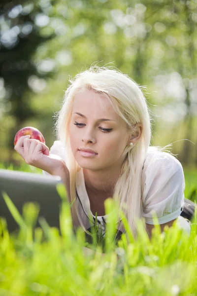 Jonge vrouw met laptop liggen op het gras — Stockfoto