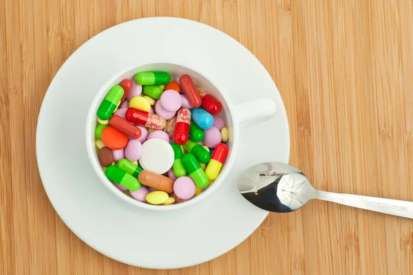 Cup with multicolored tablets and capsules — Stock Photo, Image
